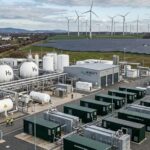 Elektrolyseanlage zur Erzeugung von grünem Wasserstoff mit Windkraftanlagen im Hintergrund